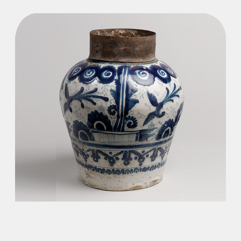 A white jar painted with dark blue ornamental patterns and a brown iron rim.
